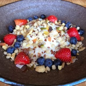 Porridge with seeds, nuts, fresh strawberries and blueberries in a bowl.