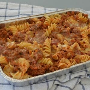 Spiral pasta and a tomato based meat sauce pasta bake in a rectangular baking dish resting on a tea towel