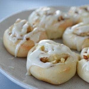 A plate of baked scrolls with apple and cinnamon inside, and a white icing drizzled over top.