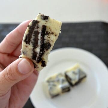A hand holding a piece of white chocolate fudge with chunks of Oreo biscuits through the fudge.