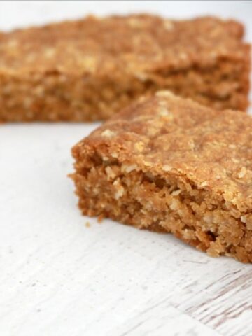 Two bars of a slice made with rolled oats on a bench.