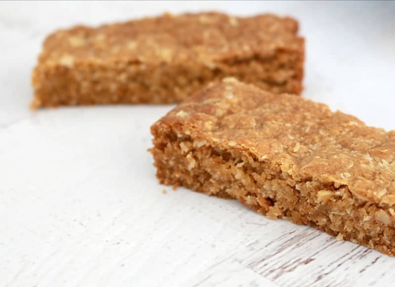 Two bars of a slice made with rolled oats on a bench.