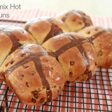 A batch of six Hot Cross Buns with a chocolate cross on top and chocolate chips inside.