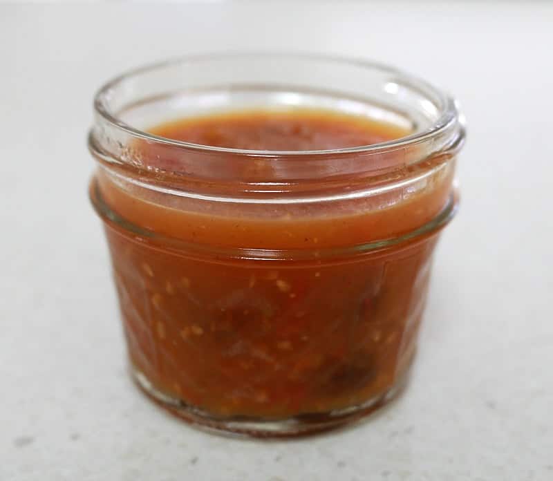 A small glass jar filled with tomato chutney.