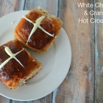 Two Hot Cross Buns made with chocolate and cranberries, served on a plate.