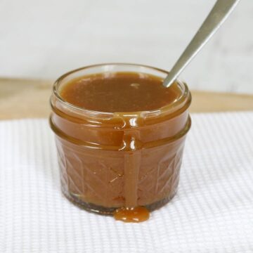 Caramel sauce in a small glass jar with some sauce drizzling down the front of it.