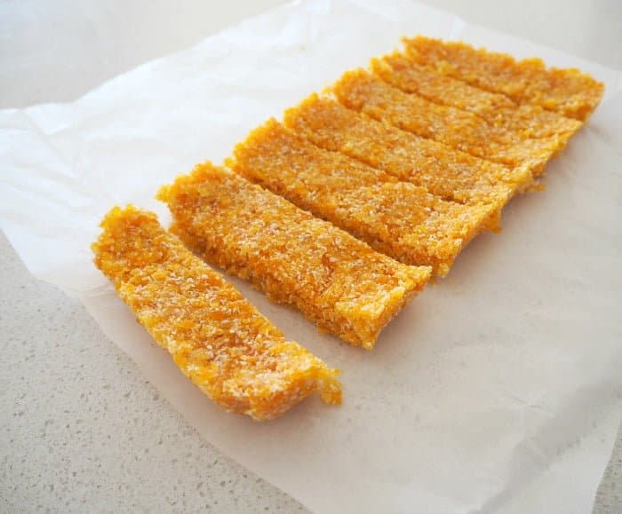 An apricot and coconut slice cut into bars, and resting on baking paper.