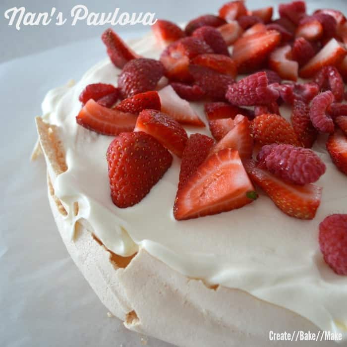 A pavlova topped with whipped cream and cut strawberries with text - Nan\'s Pavlova.