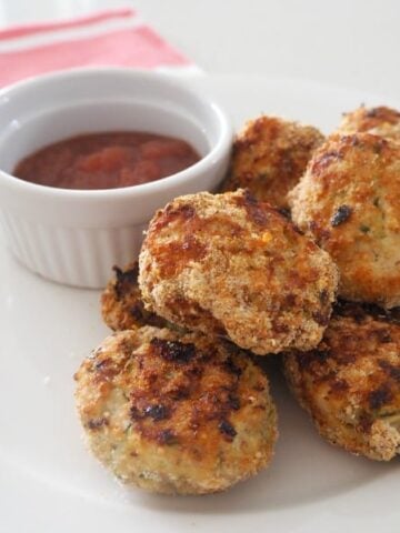 Crunchy chicken and zucchini nuggets in a pile with a bowl of relish beside.