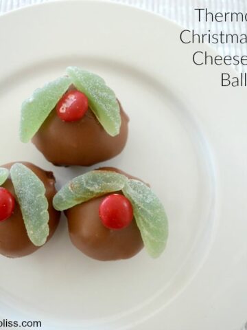 Three mini cheesecake balls coated in chocolate and decorated to resemble holly on a Christmas pudding.