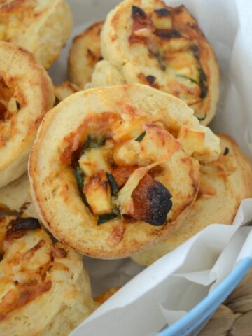 A basket filled with baked golden scrolls with spinach, feta and tomato rolled through them.