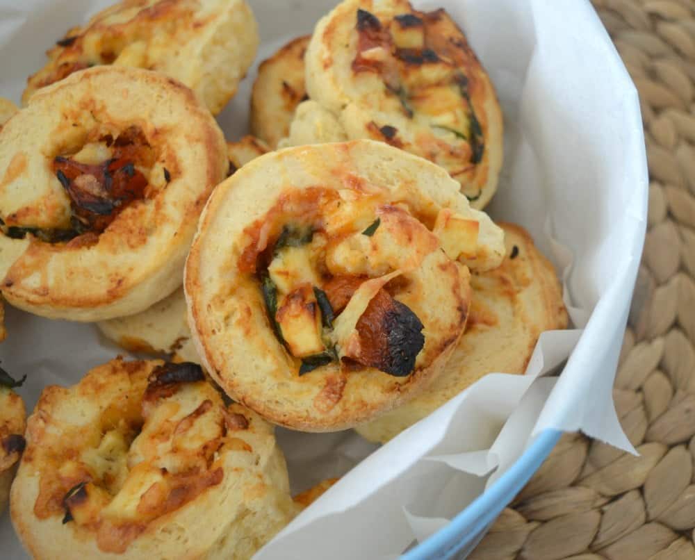 A basket filled with baked golden scrolls with spinach, feta and tomato rolled through them.