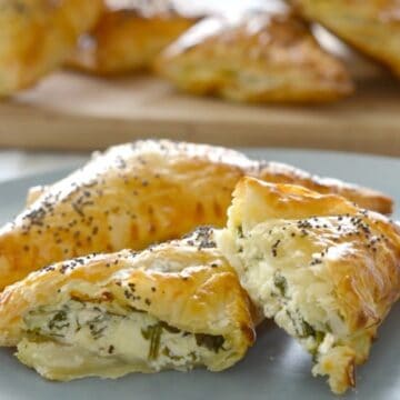 Golden pastry triangles sprinkled with poppy seeds, with one split to reveal a cheese and spinach filling.