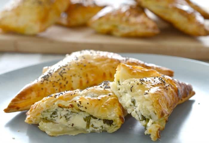 Golden pastry triangles sprinkled with poppy seeds, with one split to reveal a cheese and spinach filling.