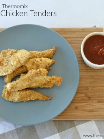Crumbed golden chicken tenders on a plate with a bowl of tomato sauce beside.