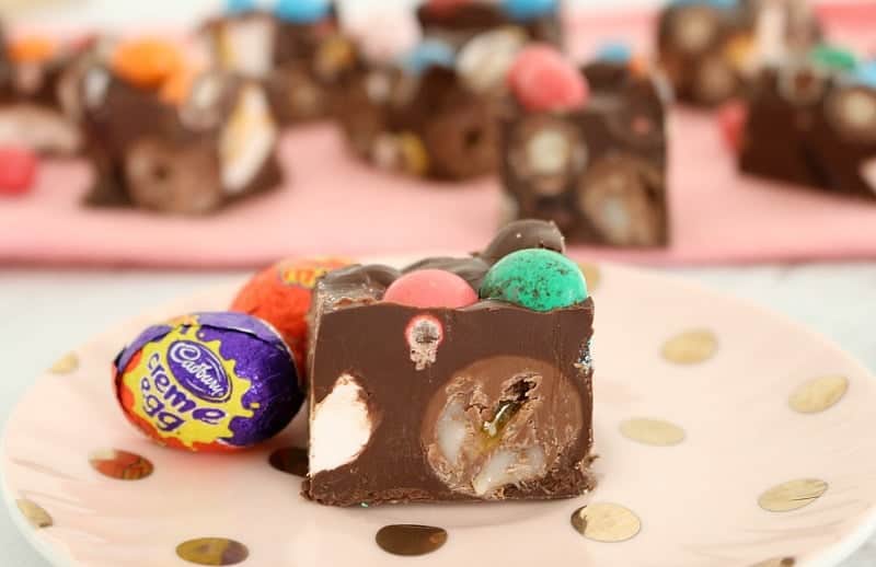A close up of a piece of Rocky Road filled with creme eggs and mini coloured Easter eggs, with more Easter eggs beside.