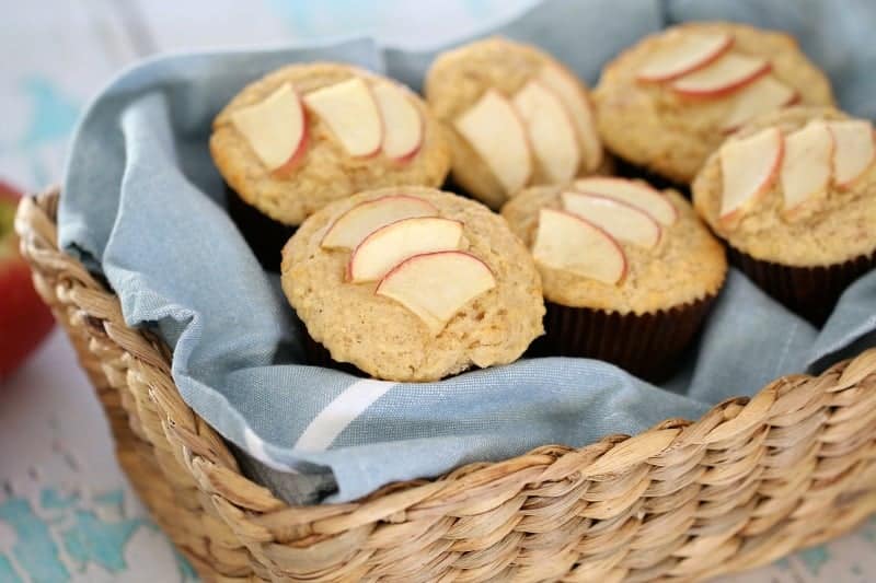 A basket filled with muffins in cases, with slices of apple baked on top.