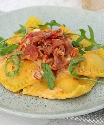 A grey dish filled with a serve of ravioli made with pumpkin and garnished with rocket leaves and crispy prosciutto.