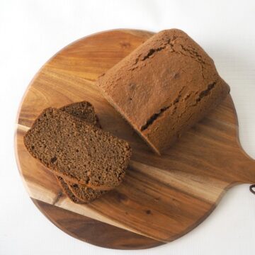 A gingerbread loaf with two slices cut, resting on a round wooden serving board.