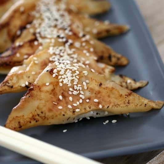 A close up of golden baked pastry triangles sprinkled with sesame seeds, lined up on a serving dish.