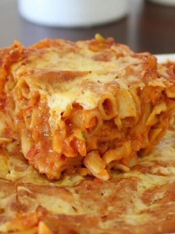 A close up of a tomato based pasta bake with lots of vegetables and cheese cooked through it.