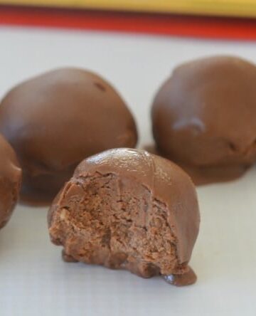 A close up of cheesecake balls made with Toblerone and coated in chocolate, with the front one half eaten to show filling.