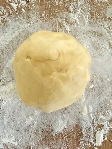 An overhead shot of a ball of shortcrust pastry on a lightly floured board.
