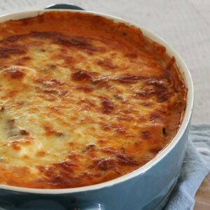 A round blue baking dish filled with moussaka  baked with a golden cheese topping.