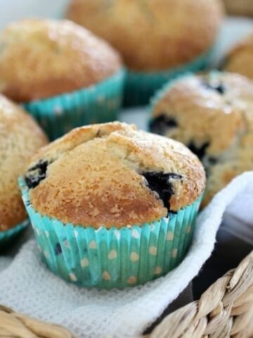 A basket filled with a batch of blueberry muffins in cases.