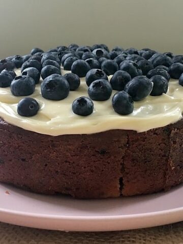 Blueberries and white frosting over the top of a round blueberry and lemon cake.