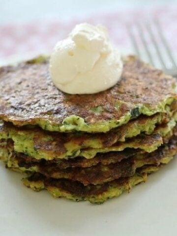 A stack of zucchini fritters topped with a dollop of sour cream.