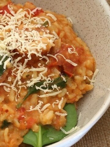 Creamy risotto made with cherry tomatoes and chorizo, resting on baby spinach leaves in a bowl.