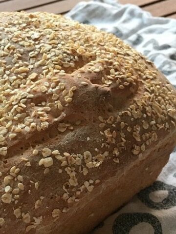 A close up of a loaf of bread with oats baked on top, resting on a tea towel.