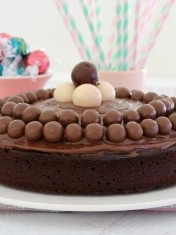 A round chocolate cake with chocolate frosting, decorated with Malteser balls and white Lindt balls on top.