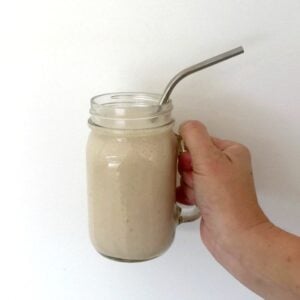 A glass jar with a handle and straw in it, filled with a creamy chocolate smoothie.