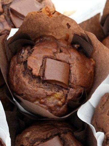 Chocolate muffins wrapped in baking paper with a chunk of chocolate on the top of each.