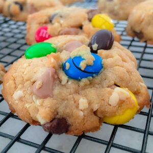 Cookies loaded with colourful M&M's cooling on a black wire tray.