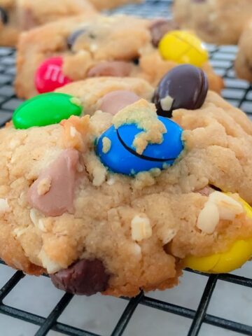 Cookies loaded with colourful M&M's cooling on a black wire tray.