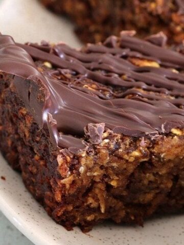 A close up of a square of slice made with rolled oats and dates, and drizzled with dark chocolate.