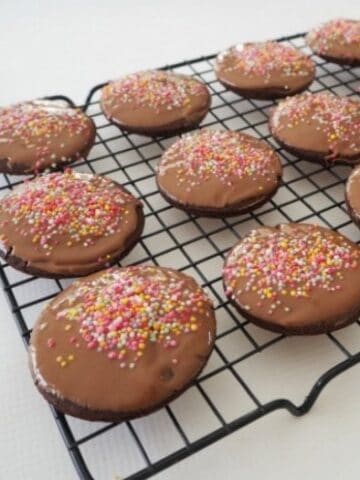 Chocolate biscuits with sprinkles on top cooling on a black wire rack.