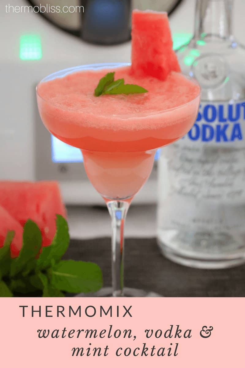 A cocktail glass filled with a watermelon coloured cocktail and mint garnish, with a bottle of vodka in the background.