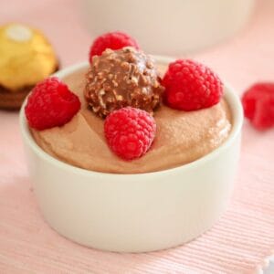 A Ferrero Rocher chocolate and fresh raspberries on top of a chocolate mousse served in a small white ramekin dish.