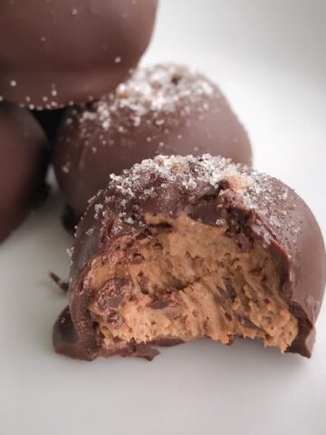 A pile of chocolate coated balls with the front one half eaten showing the chocolate cheesecake texture inside.