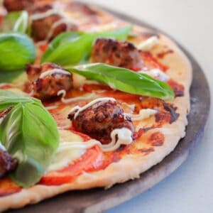 A pizza topped with chunks of pork sausage, tomato slices, melted cheese and basil leaves.
