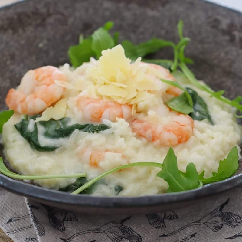 Shredded parmesan on top of a risotto filled with prawns and rocket leaves in a bowl.