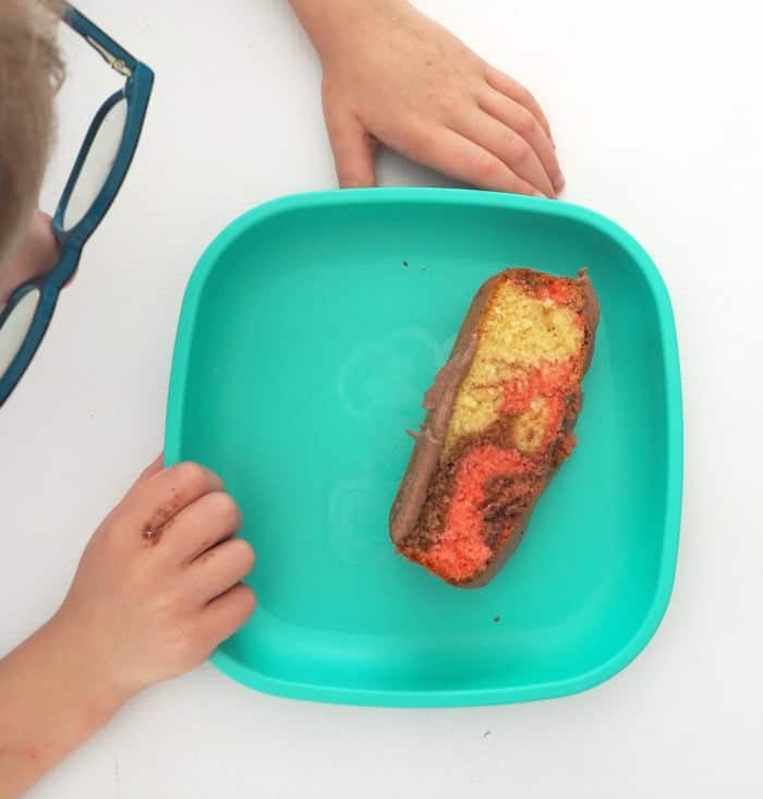 Two child\'s hands holding a blue dish with a slice of frosted marble cake inside.