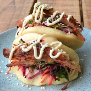 2 Bao buns with coleslaw, meat and mayonnaise, sitting on a blue plate on a wooden table.
