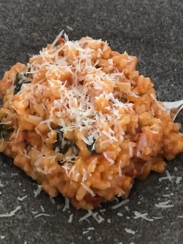 Grated parmesan on top of a tomato and bacon risotto in a bowl