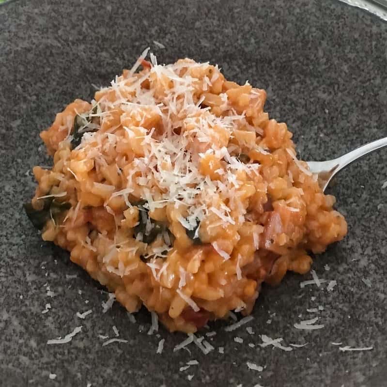 Grated parmesan on top of a tomato and bacon risotto in a bowl