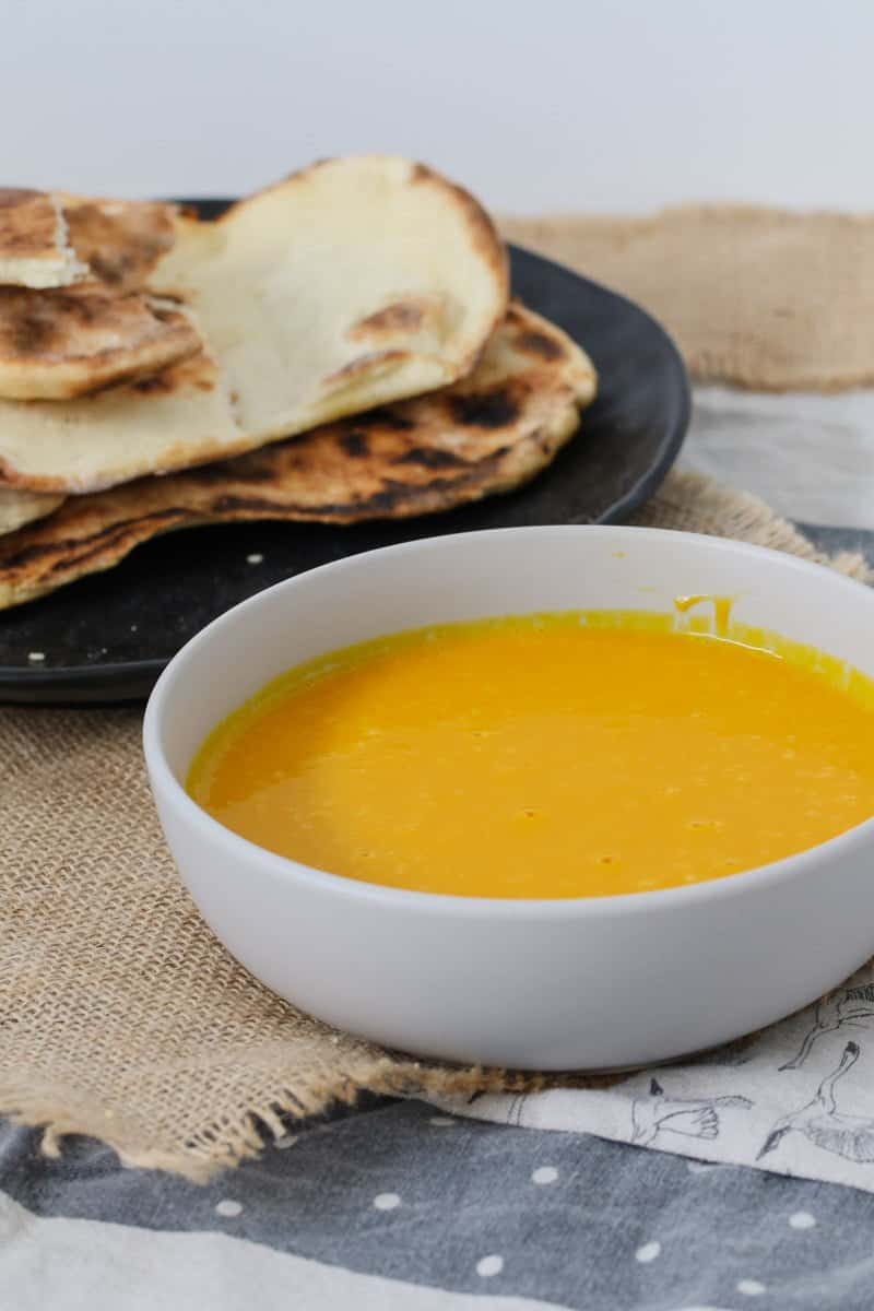 A bowl of pumpkin soup with naan bread in the background.